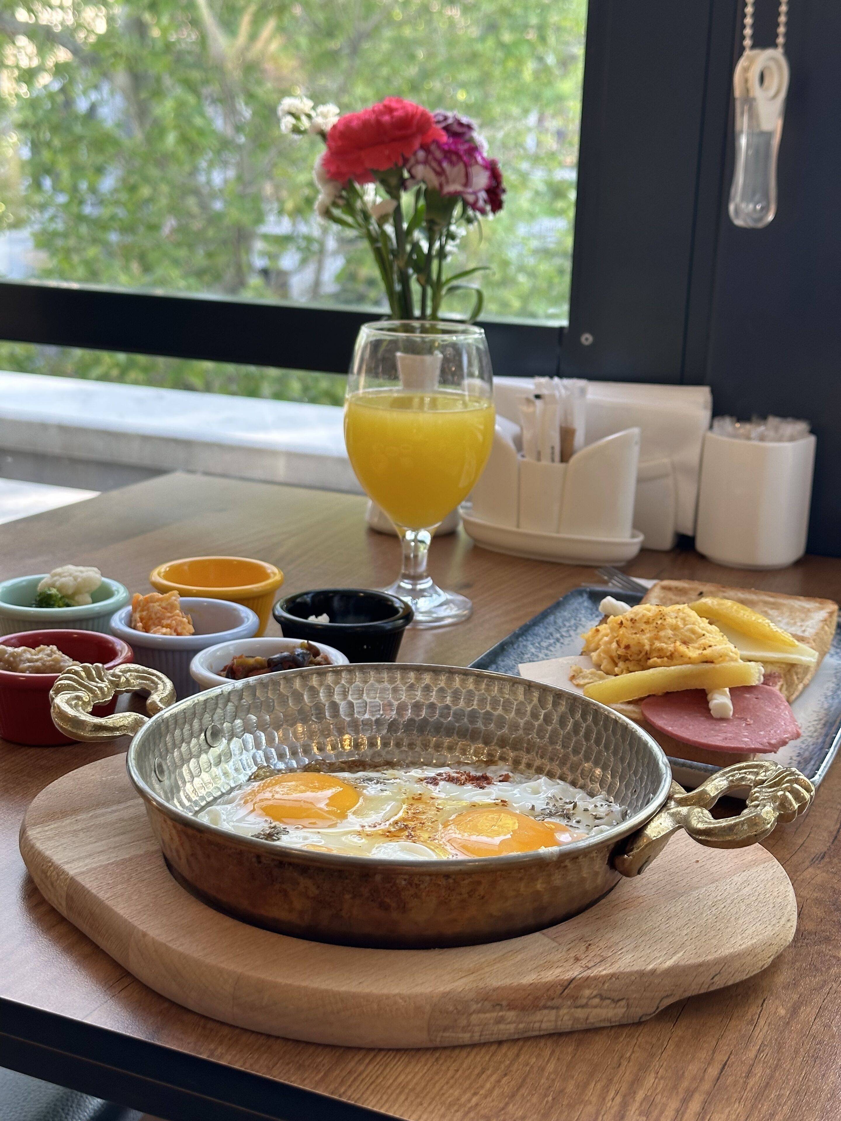 A breakfast tray with eggs, toast, ham, and a glass of orange juice on a wooden table by a window.