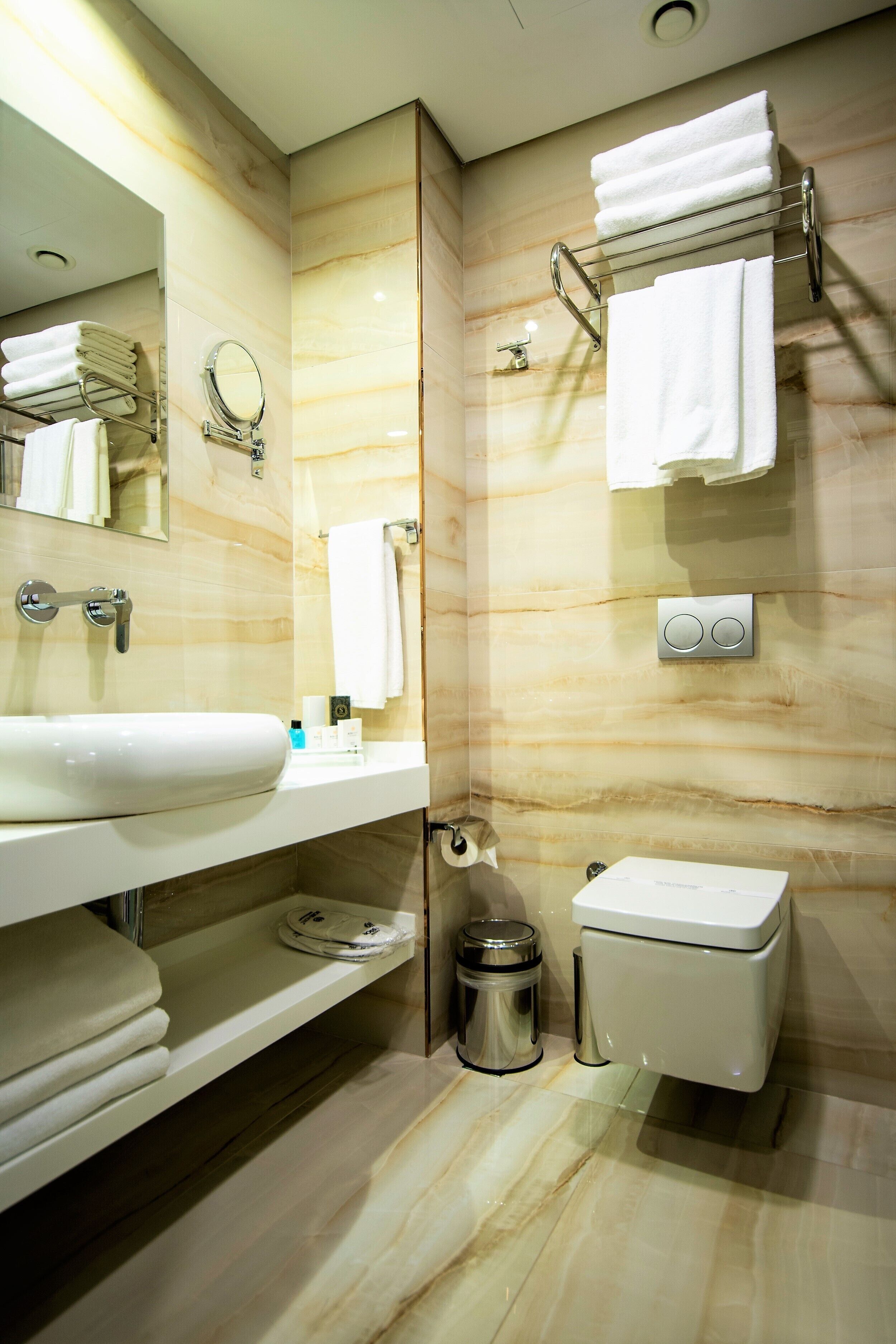 A modern bathroom with a large sink, mirror, towel rack, and toilet.