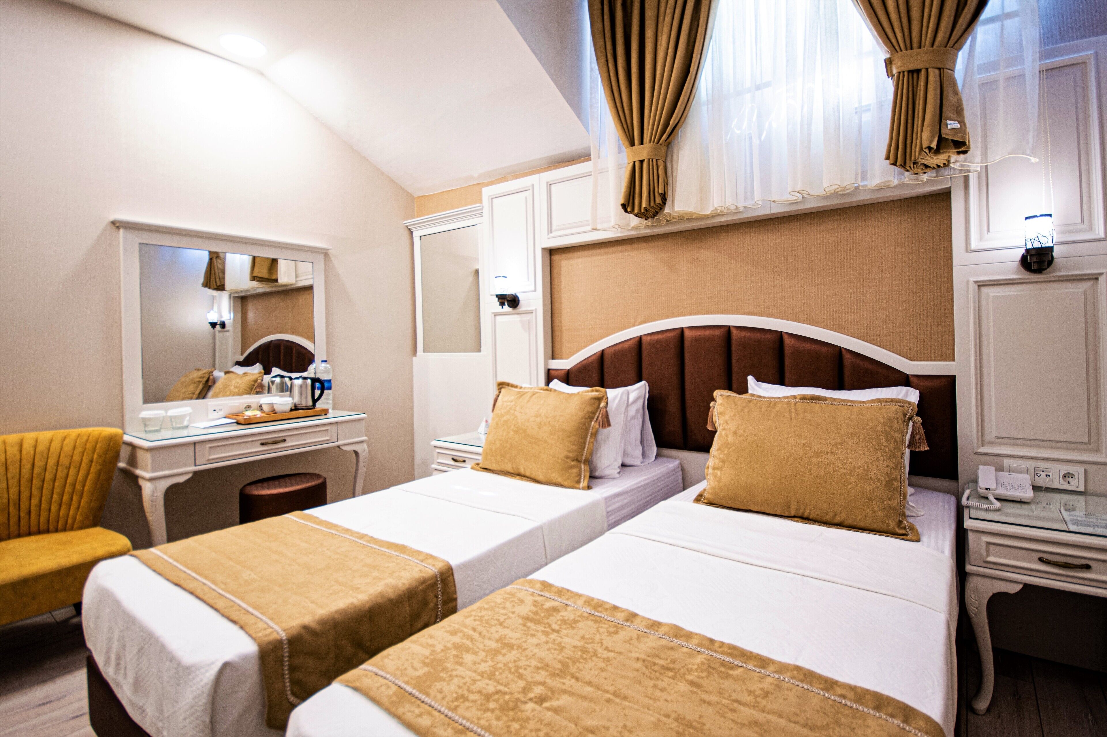 A hotel room with two single beds, a desk with a chair, a mirror, and a window with curtains.