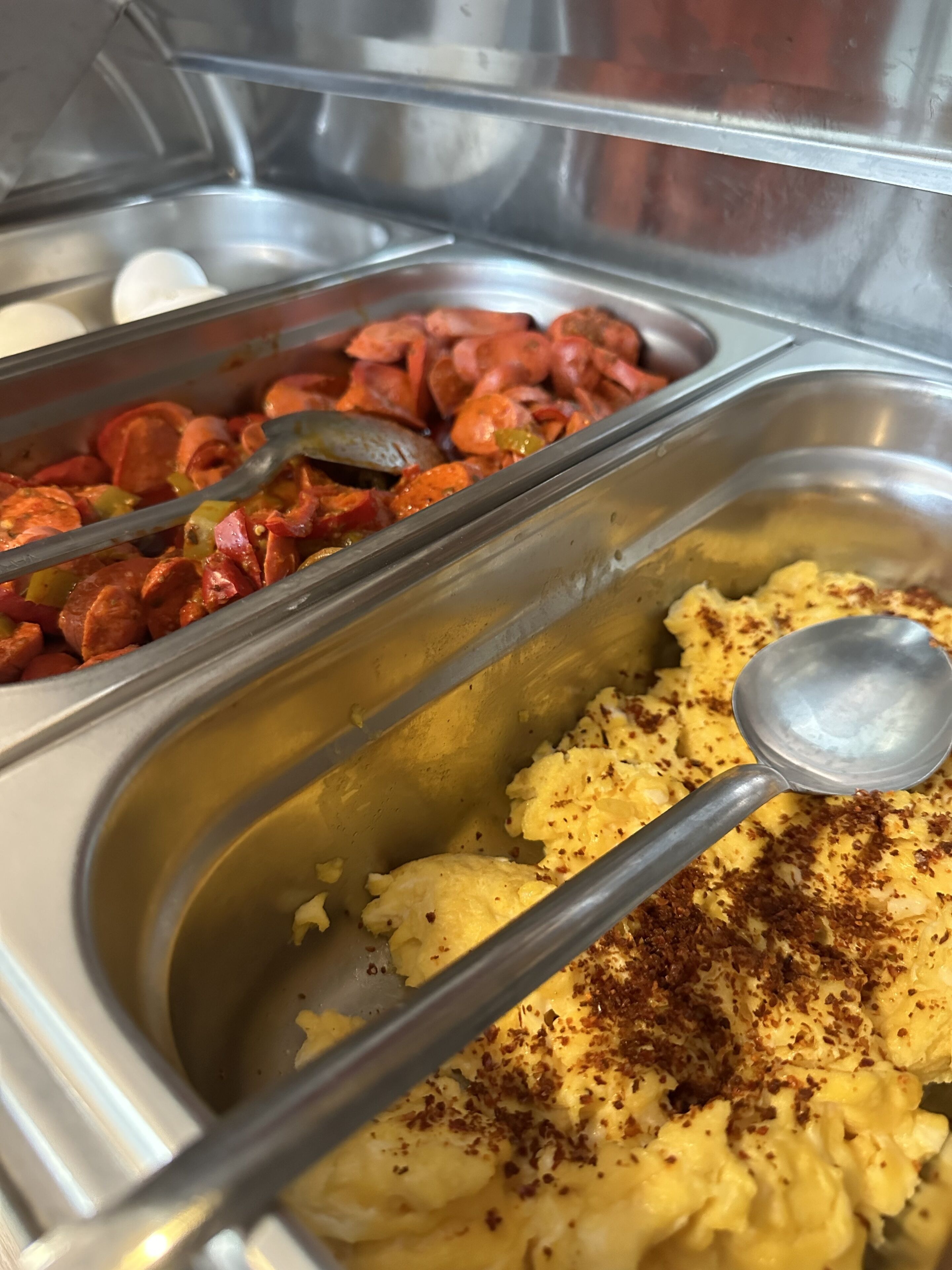 Un buffet con diversi piatti, tra cui uova strapazzate e salsiccia.