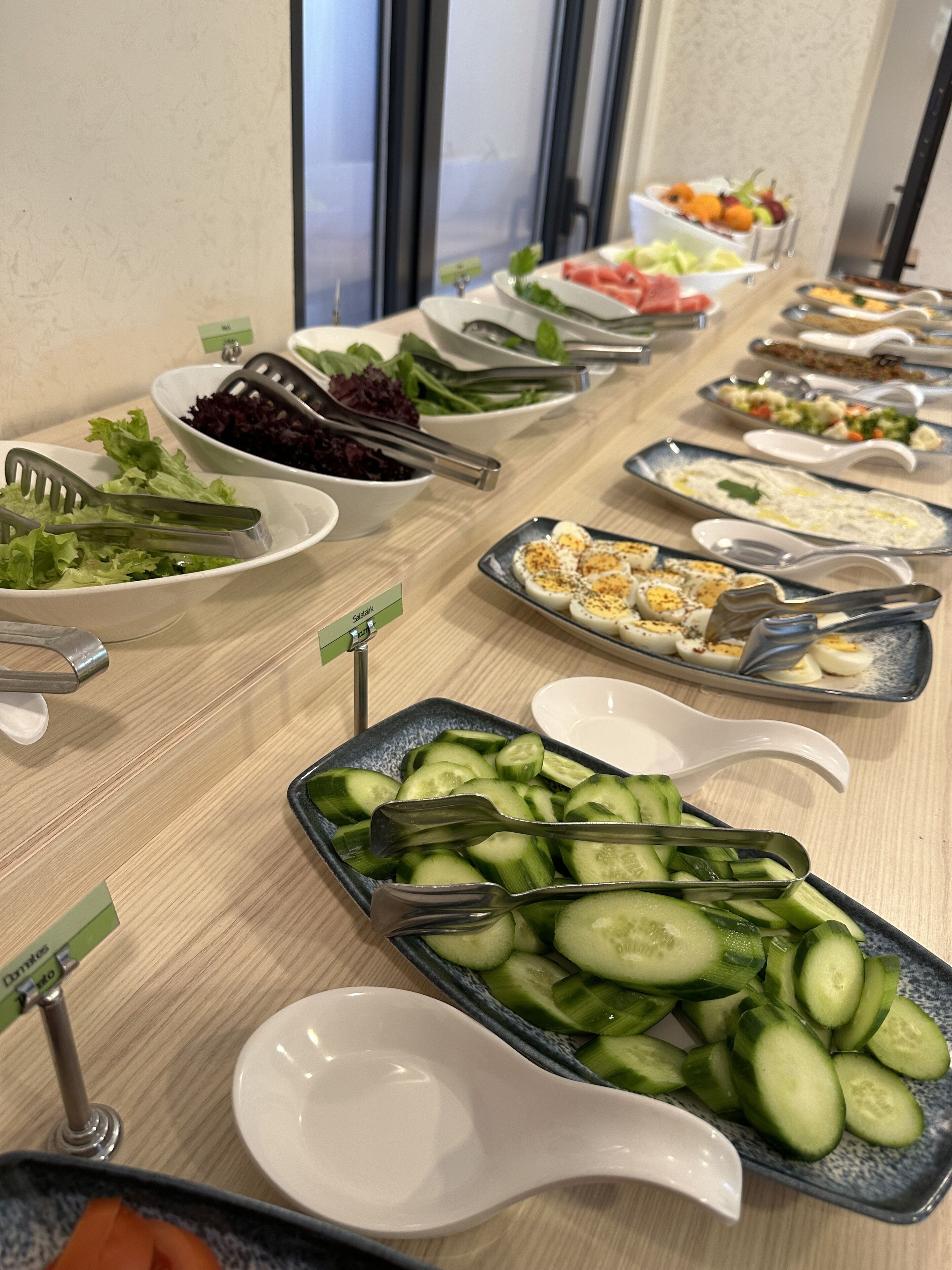 A buffet table with various food items including salads, cucumbers, and eggs.