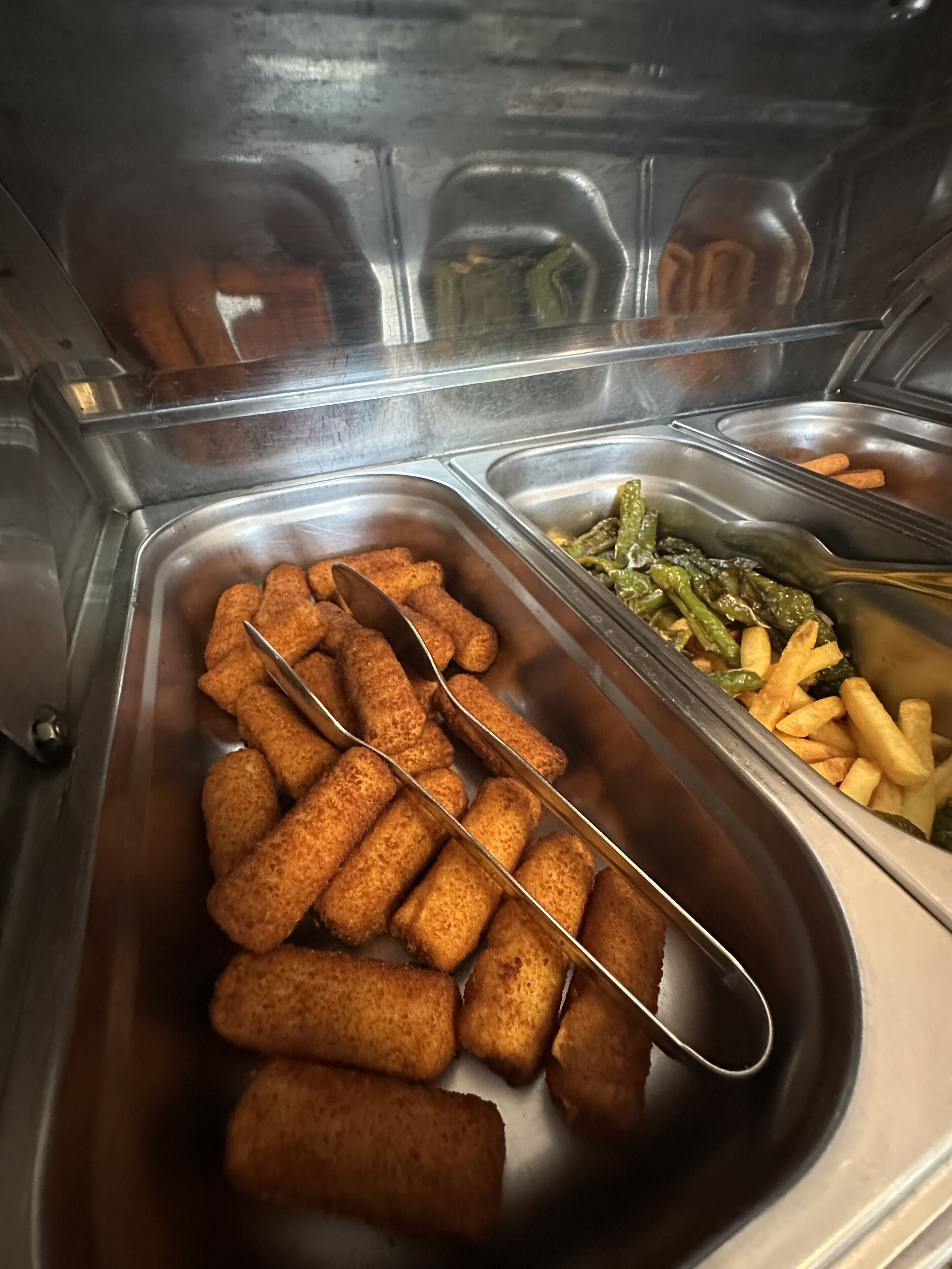 A buffet with trays of food including croquettes, green beans, and fries.