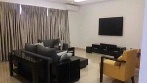 A modern living room with a sectional sofa, a yellow armchair, and a flat-screen TV mounted on the wall. - Koza Town (Lagos)