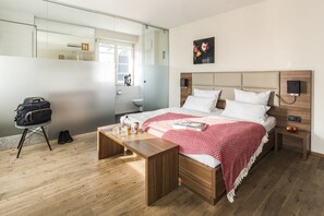 Une chambre d’hôtel moderne avec un lit en bois, une table de chevet, une commode, un miroir et une vue sur la salle de bain.