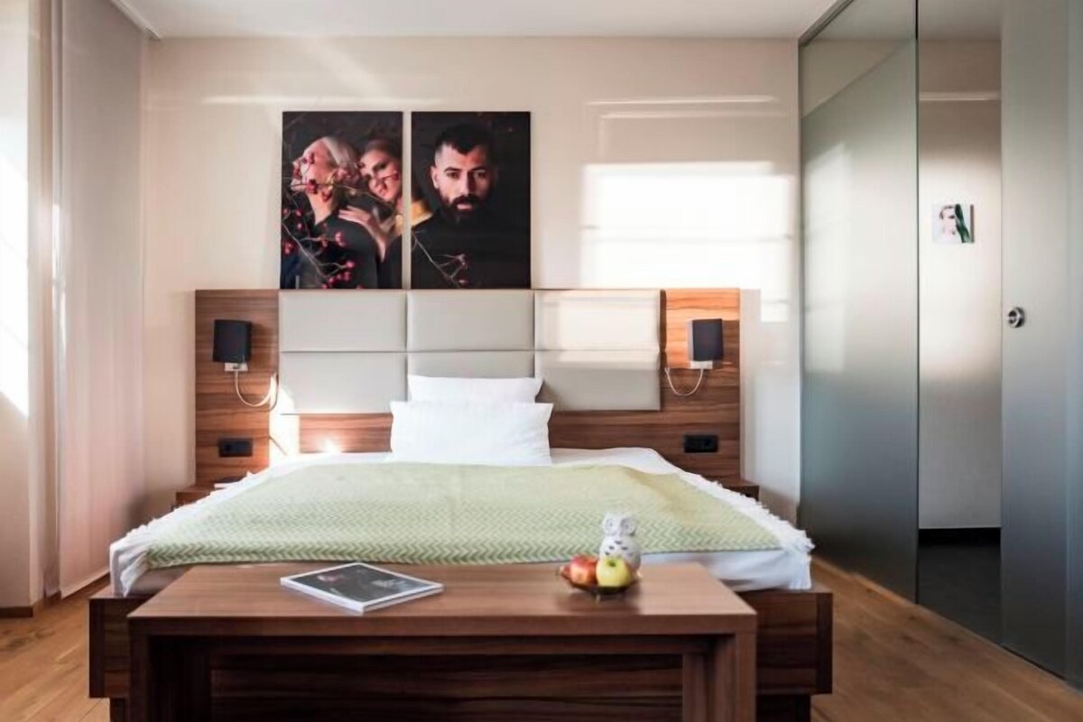 Un dormitorio moderno con una cama de madera, una mesita de noche con lámpara y un televisor montado en la pared.
