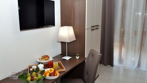 Habitación de hotel con un escritorio de madera, una silla, un televisor, una lámpara y una ventana con cortinas.