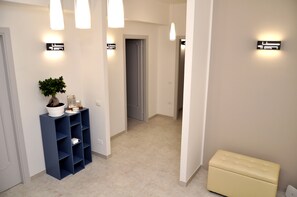 A hallway with a potted plant, a blue shelving unit, and a cream-colored bench. - B&B Kalurya (Lecce)