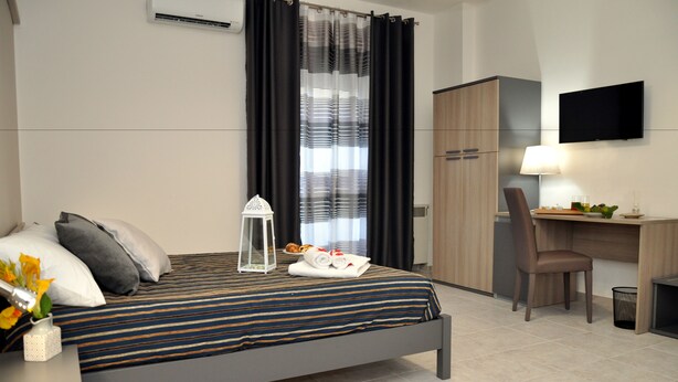 Una habitación de hotel moderna con cama, escritorio, silla, televisor y ventana con cortinas.