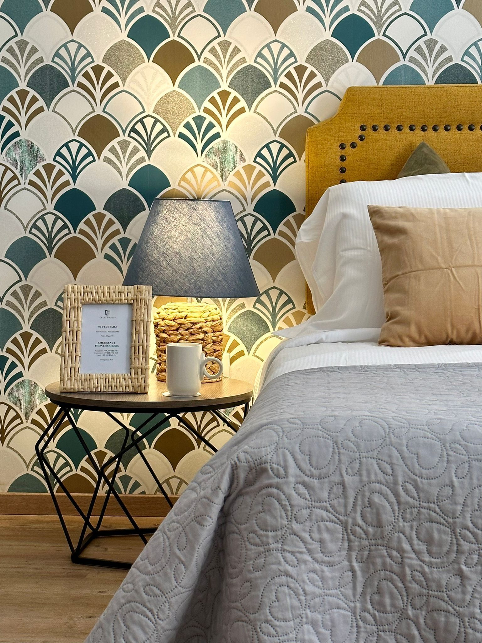 A neatly made bed with a white quilt, a bedside table with a lamp, a framed sign, and a woven basket.