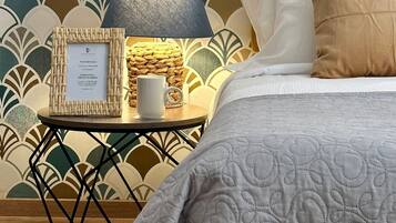 A neatly made bed with a white quilt, a bedside table with a lamp, a framed sign, and a woven basket.