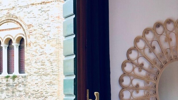 Una habitación con vistas a un edificio histórico a través de una ventana, un espejo decorativo y una puerta con picaporte de latón.