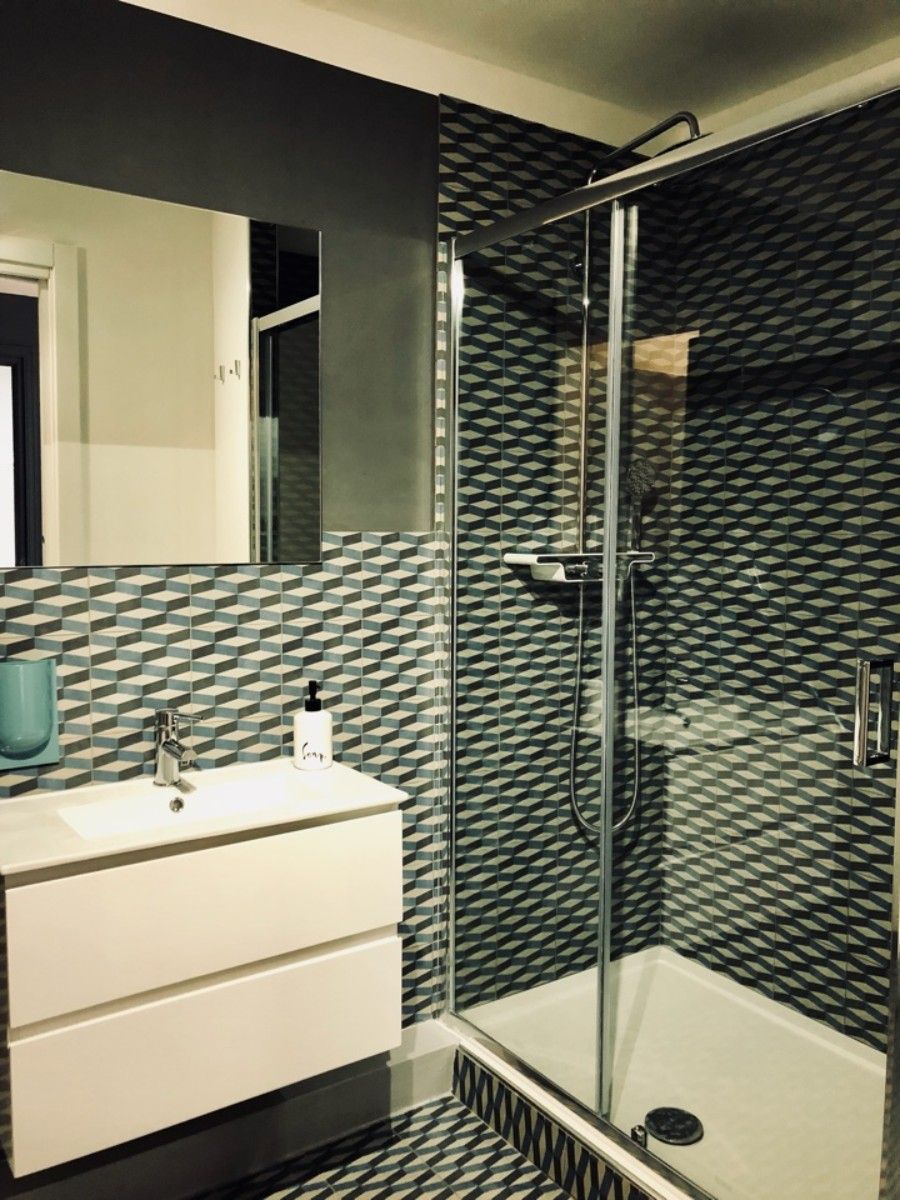 Un baño moderno con cabina de ducha de vidrio, tocador blanco con espejo y azulejos con diseño.