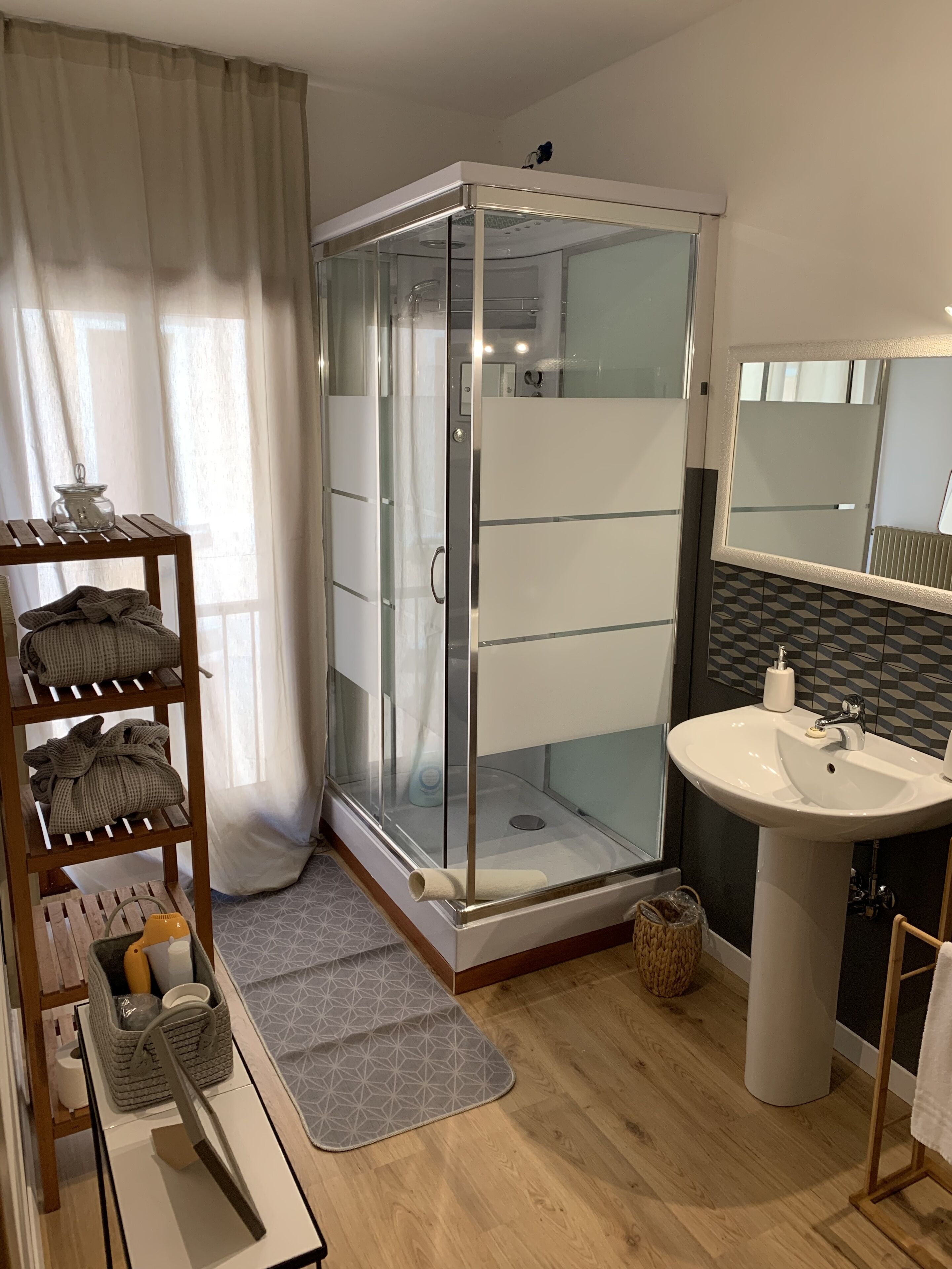 Un baño moderno con ducha de vidrio, un lavamanos blanco y un estante de madera con toallas.