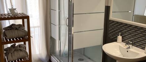 Un baño moderno con ducha de vidrio, un lavamanos blanco y un estante de madera con toallas.