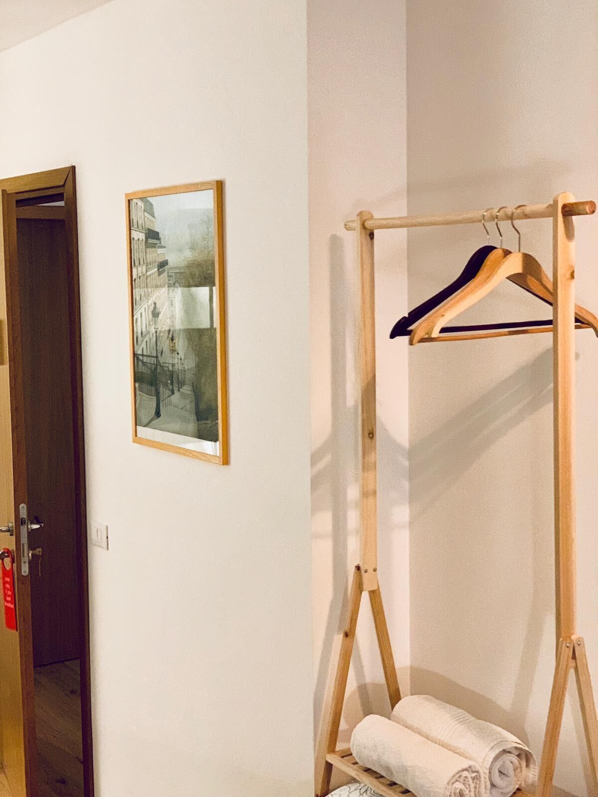 Una habitación con una puerta de madera, un cuadro en la pared y un perchero de madera con toallas.