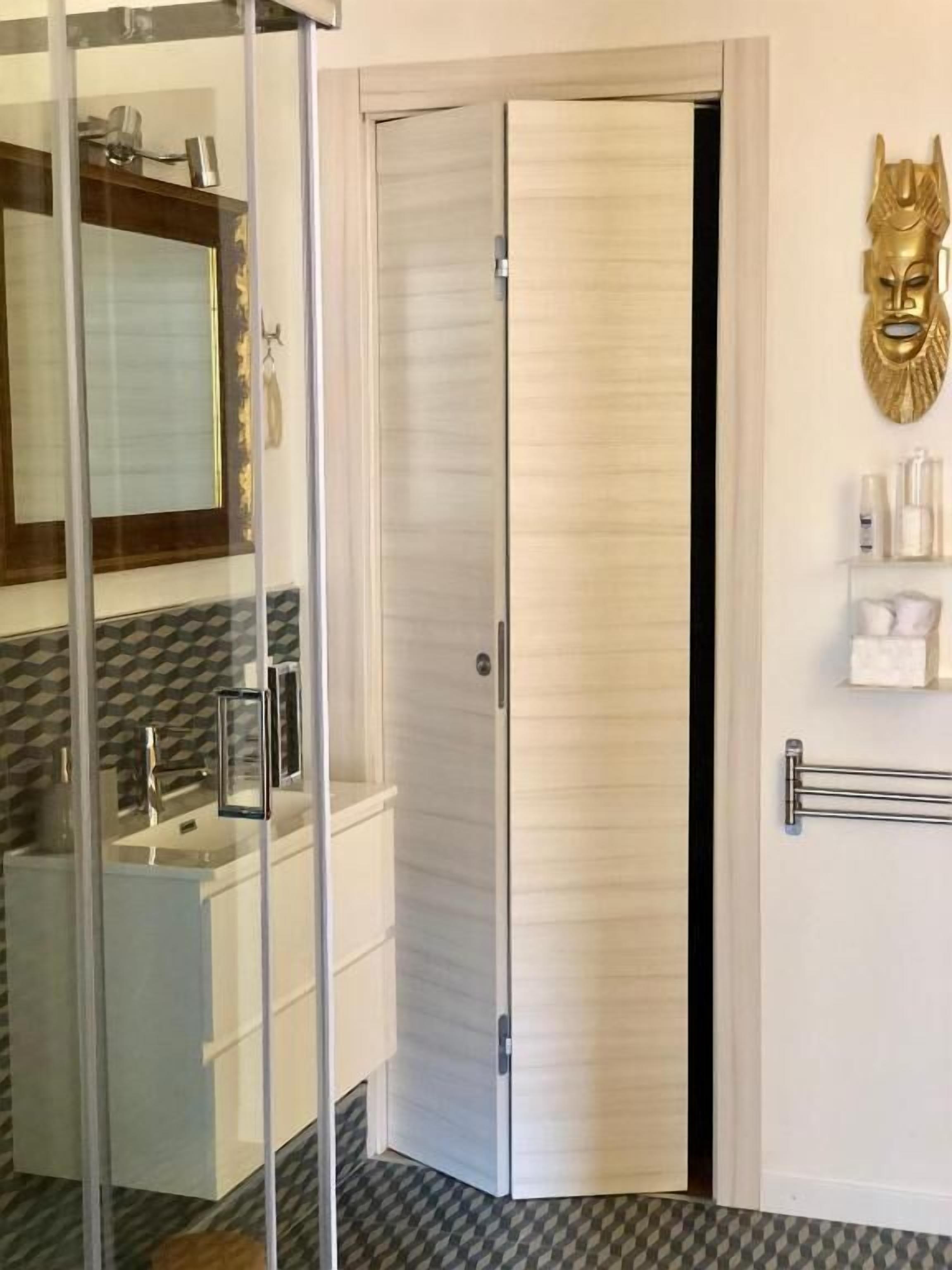 A bathroom with a glass shower enclosure, a white sink, and a gold decorative mask on the wall.