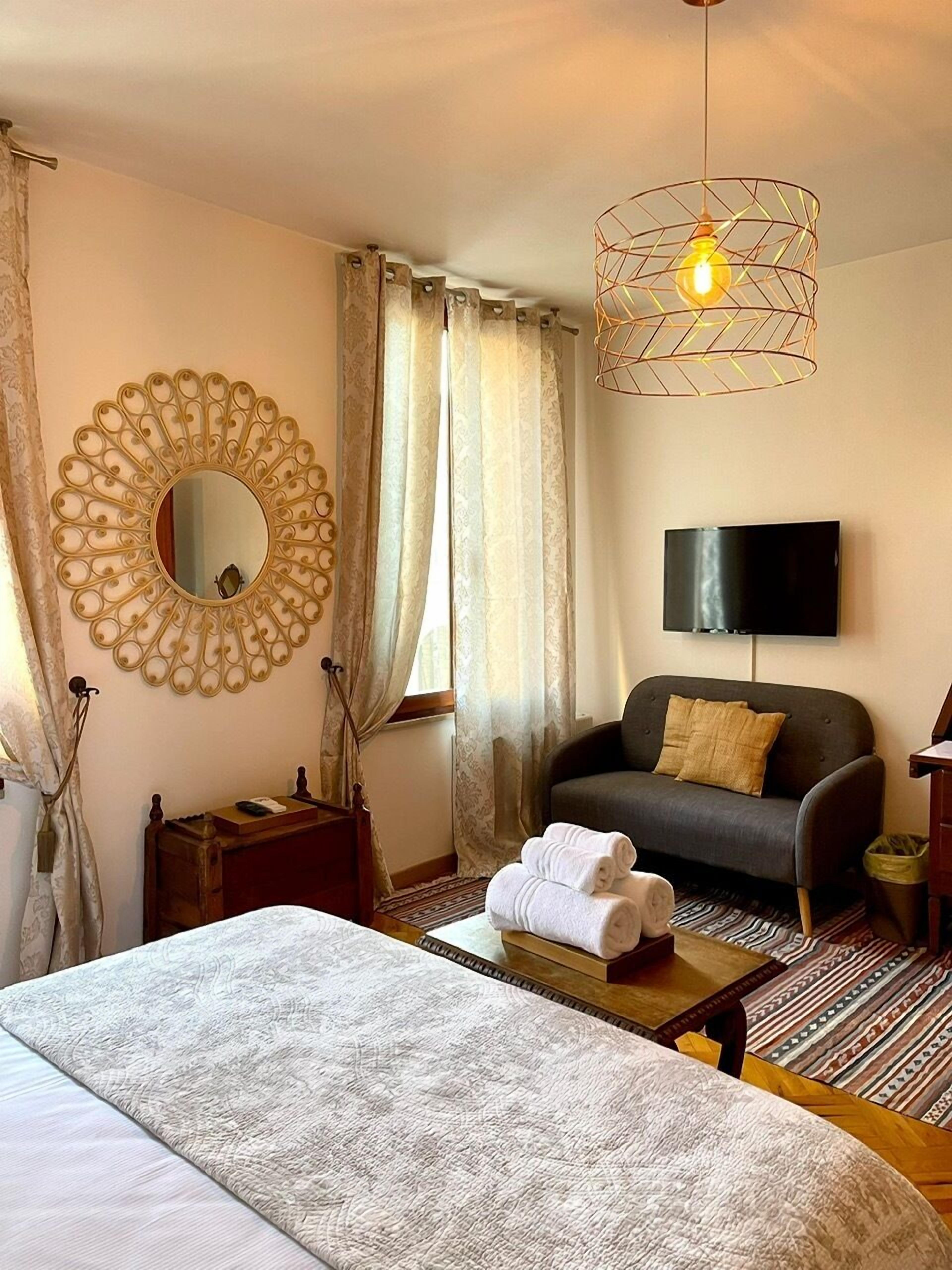 Una habitación de hotel con cama, sofá, televisor, espejo y una lámpara decorativa.