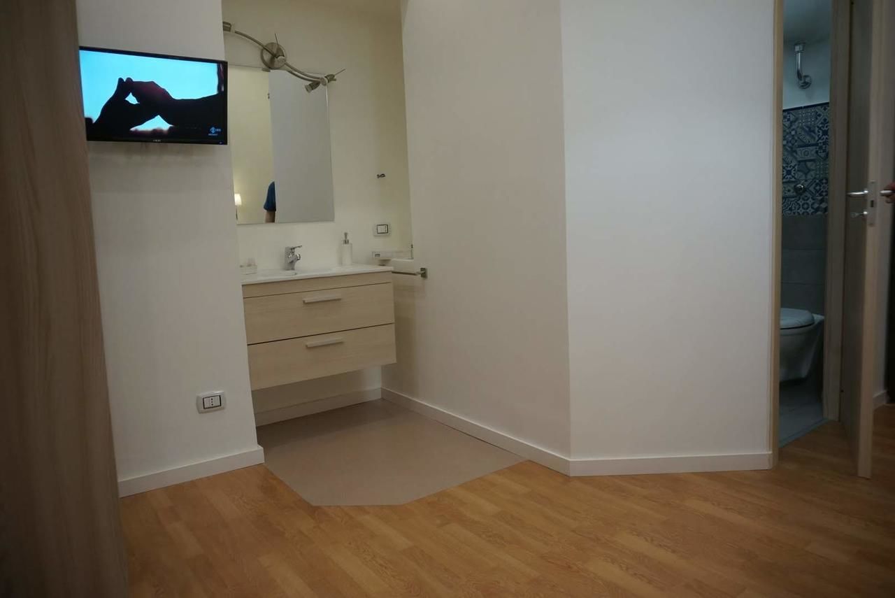 Ein modernes Badezimmer mit Holzboden, einem beigen Waschtisch, einem Spiegel und einem an der Wand montierten Fernseher.