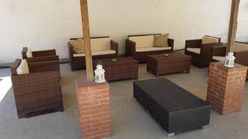 A room with wicker furniture, including sofas and a rectangular bench, supported by brick pillars.