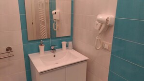 Een badkamer met een witte wastafel, een spiegel, een haardroger en een telefoon.