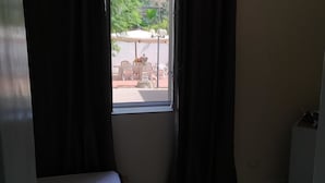Een kamer met een raam dat uitkijkt op een terras met tafels en stoelen.
