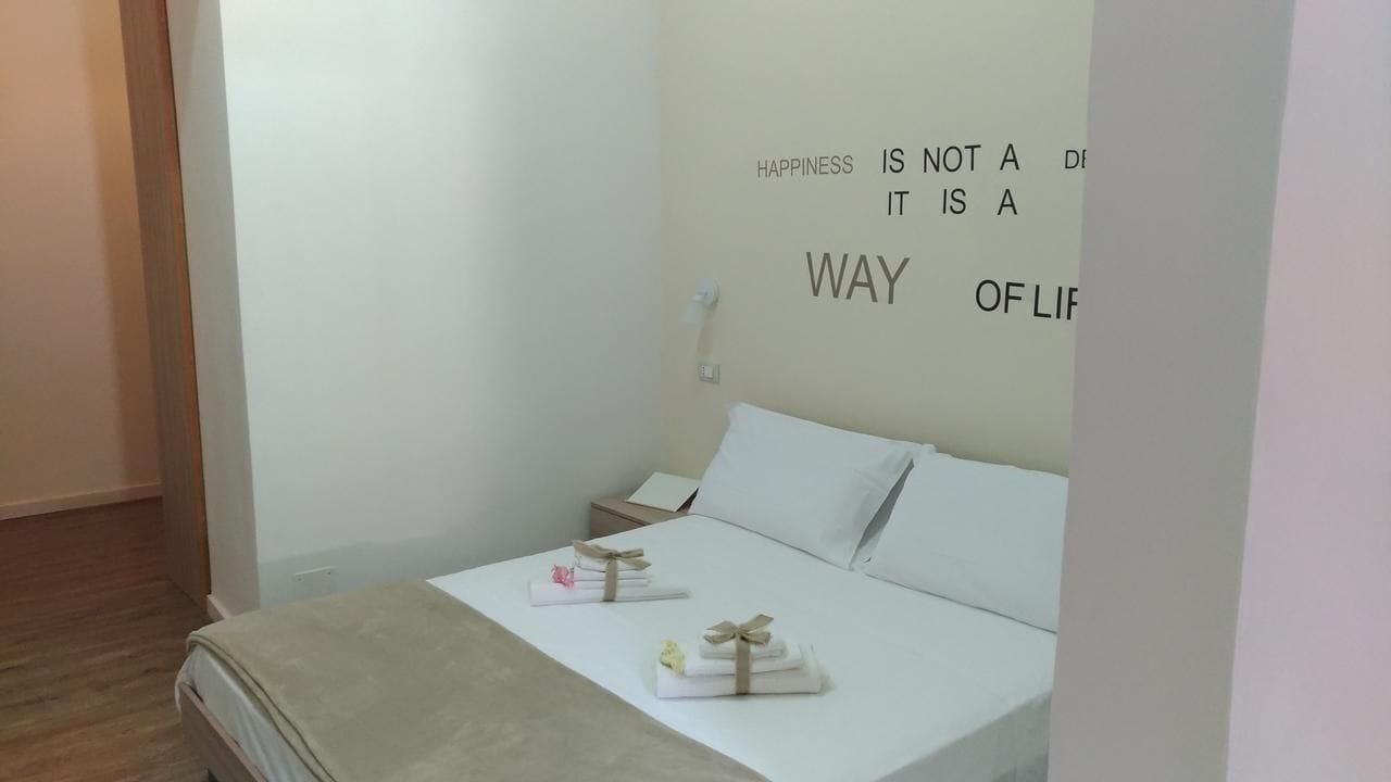 Une chambre à coucher épurée et minimaliste, avec un lit, une table de chevet et un mur orné d’une citation inspirante.
