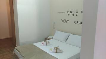 Une chambre à coucher épurée et minimaliste, avec un lit, une table de chevet et un mur orné d’une citation inspirante.