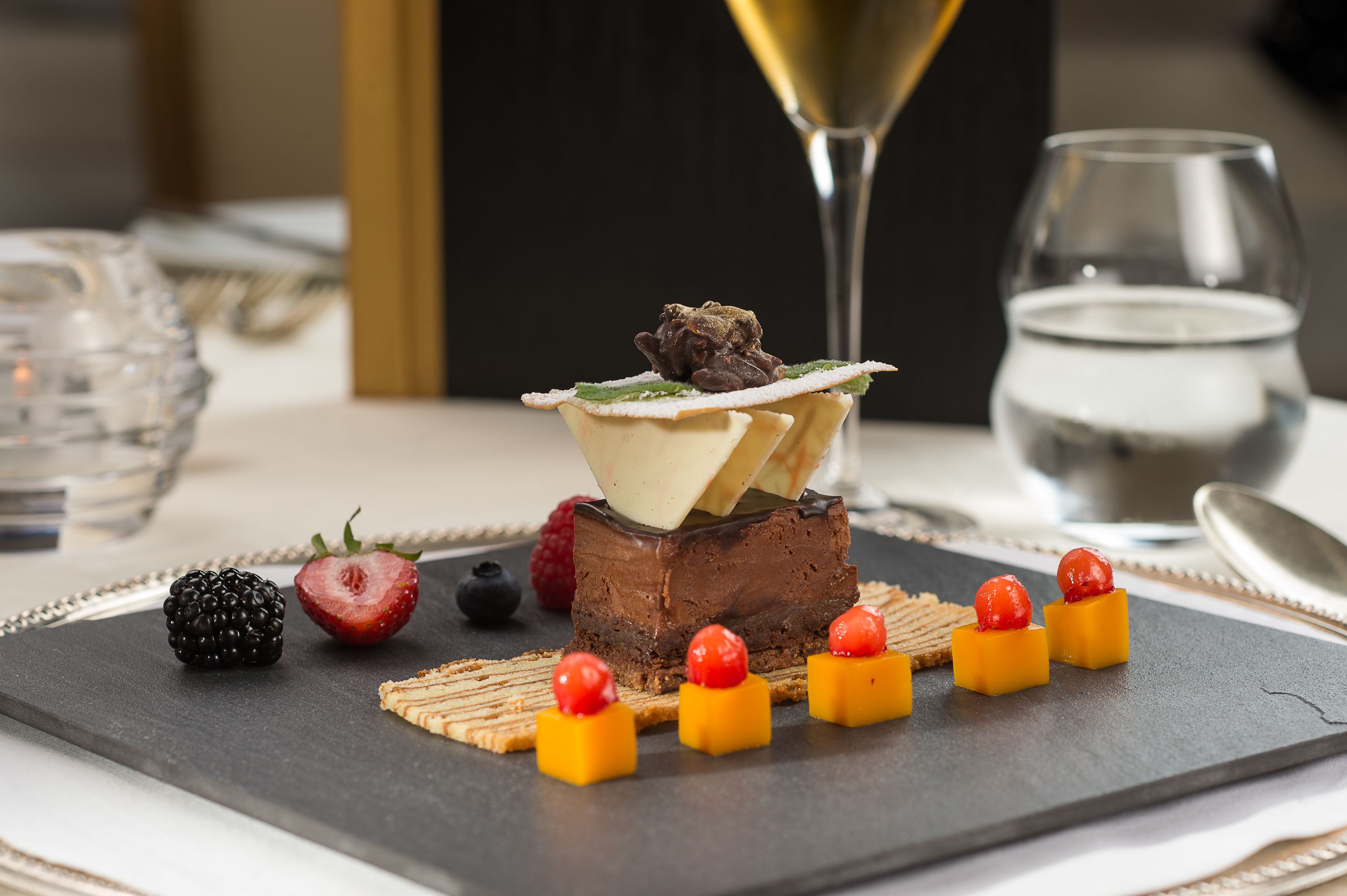 A dessert plate with a chocolate mousse cake, berries, and small cheese cubes.