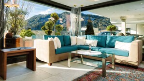 Una sala de estar moderna con un sofá color turquesa, una mesa de centro de vidrio y vistas a un paisaje montañoso a través de amplios ventanales.