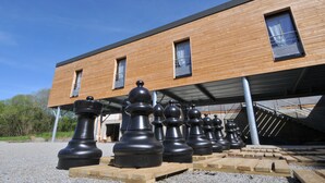 A modern building with a wooden facade and large chess pieces in front. - Auberge Des VoyaJoueurs (Monteneuf)