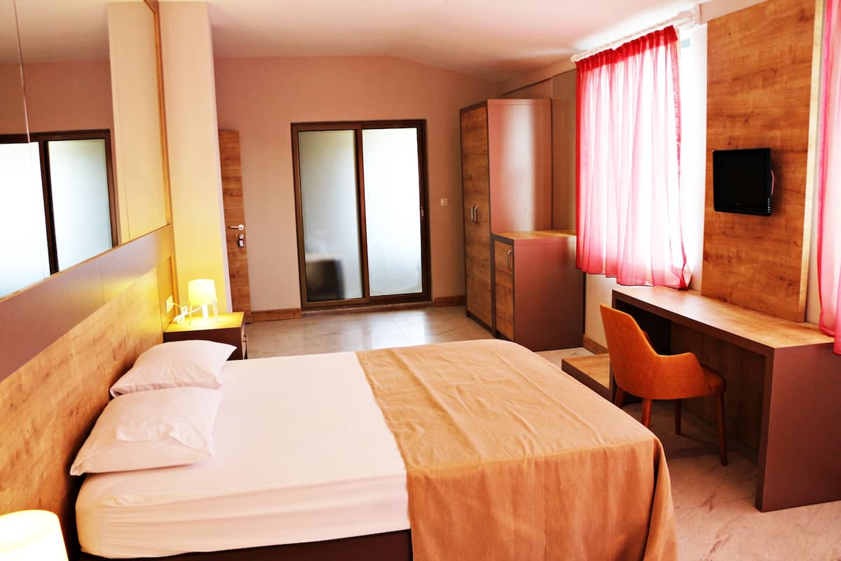 A hotel room with a bed, a desk, a chair, a TV, and a sliding door to a balcony.