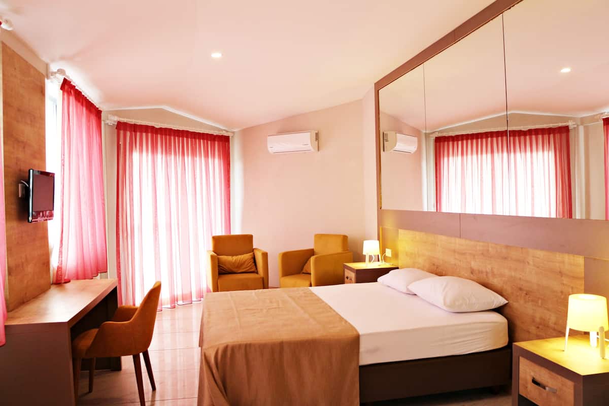 A hotel room with a bed, two chairs, a desk, a TV, and a mirror.