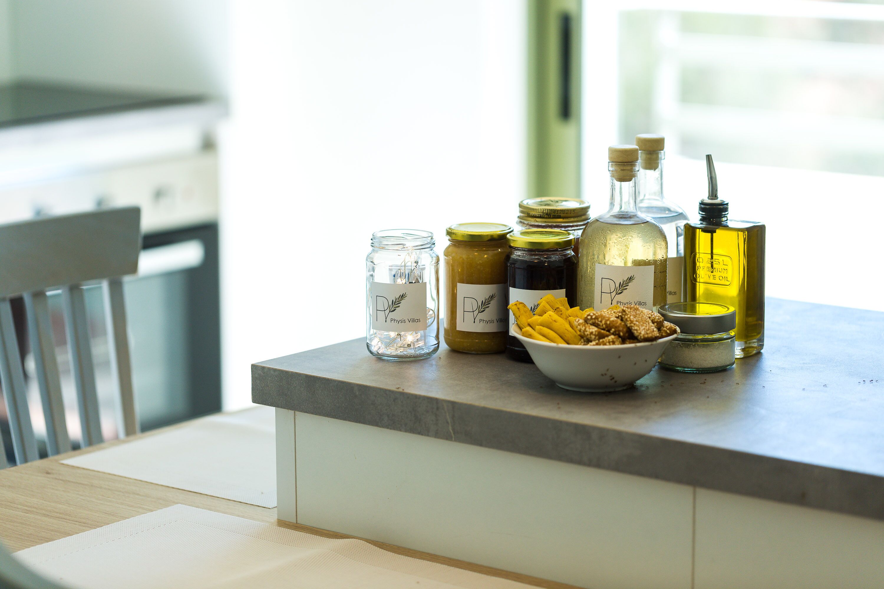 Un piano di lavoro della cucina con diversi alimenti e condimenti, tra cui vasetti, bottiglie e una ciotola di snack.