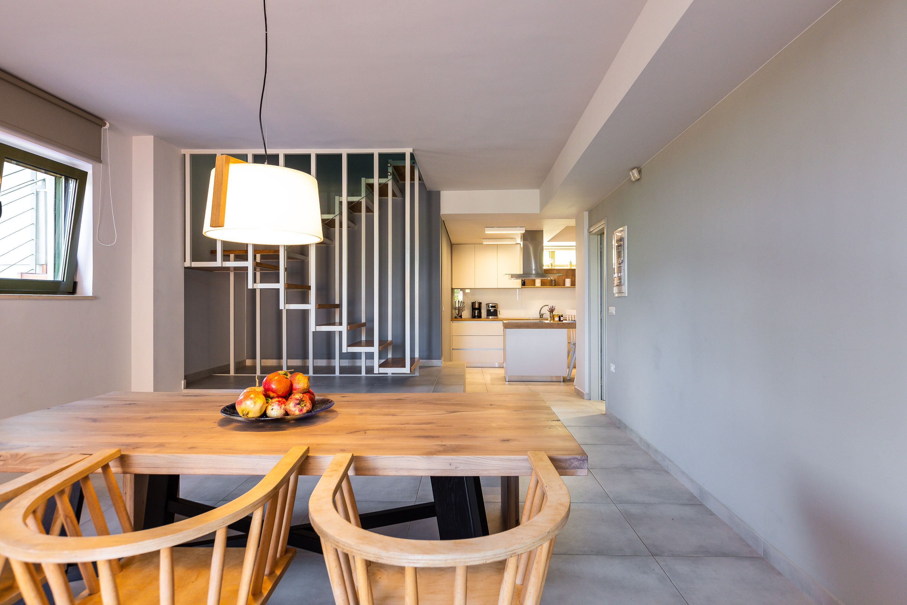 Un'area pranzo moderna con un tavolo e sedie in legno, una ciotola di frutta e una scala che conduce a un piano superiore.