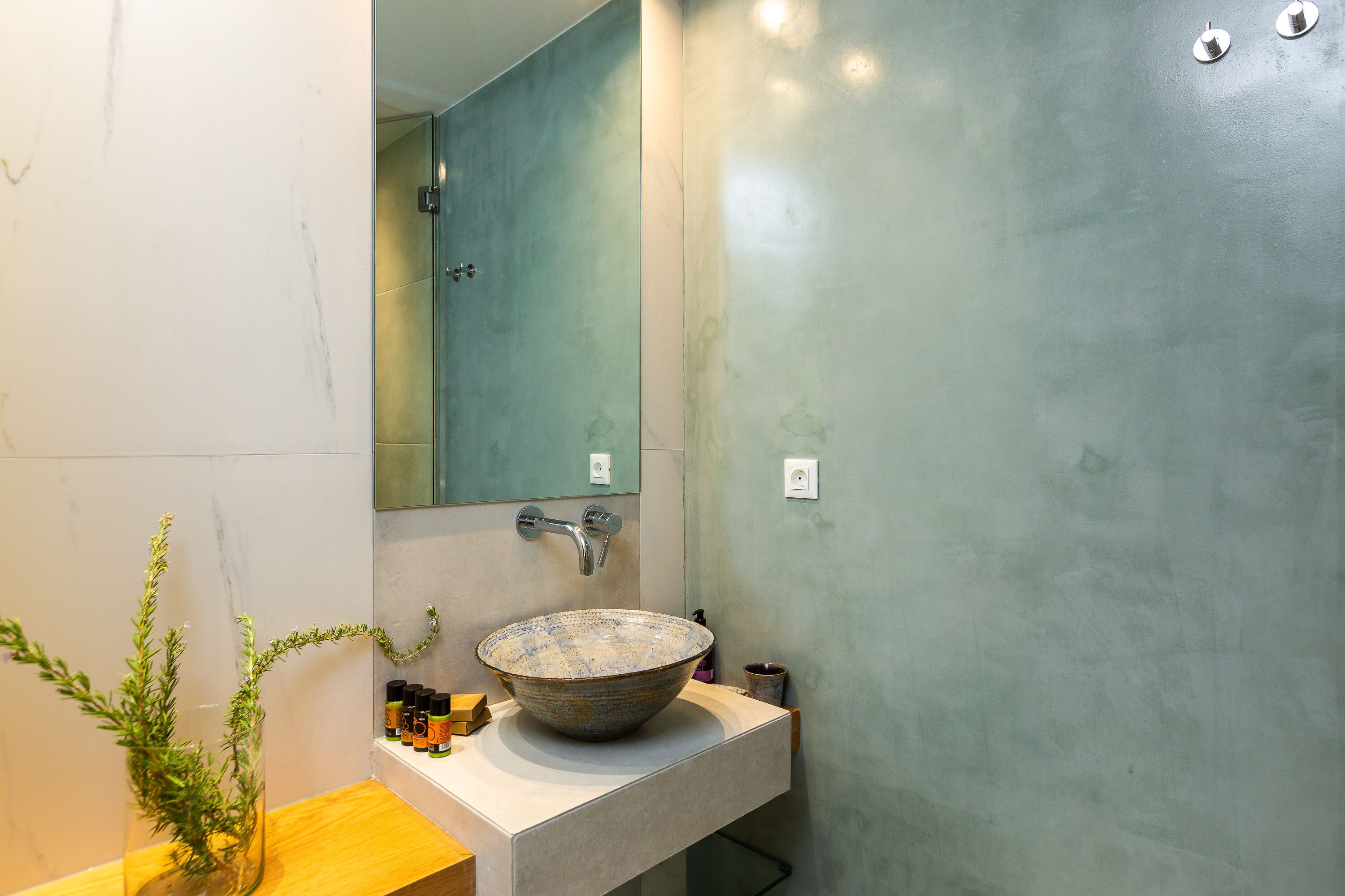 A bathroom with a large ceramic sink, a mirror, and a wooden countertop.