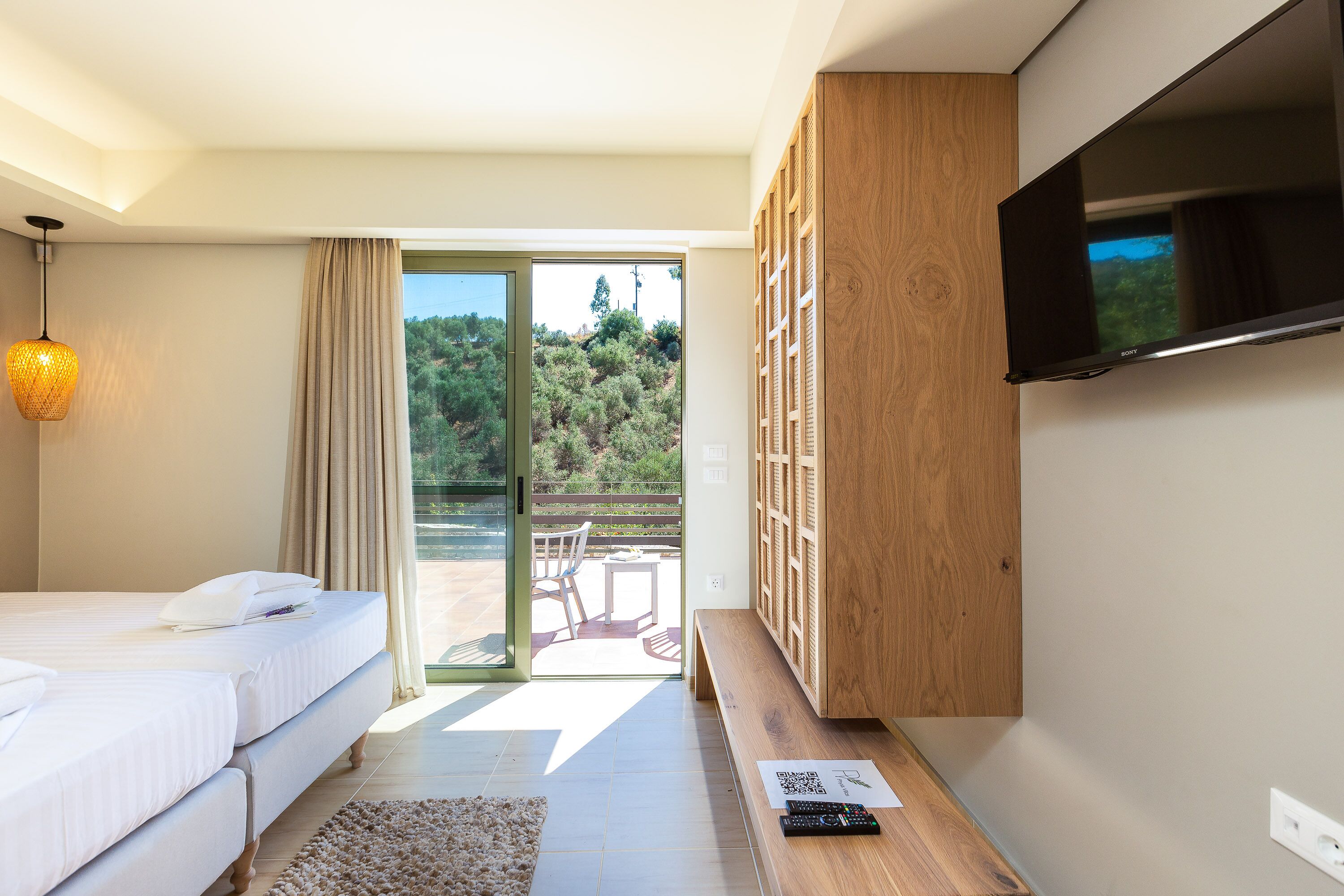 A hotel room with a bed, a TV, a wooden cabinet, and a view of the outdoors.