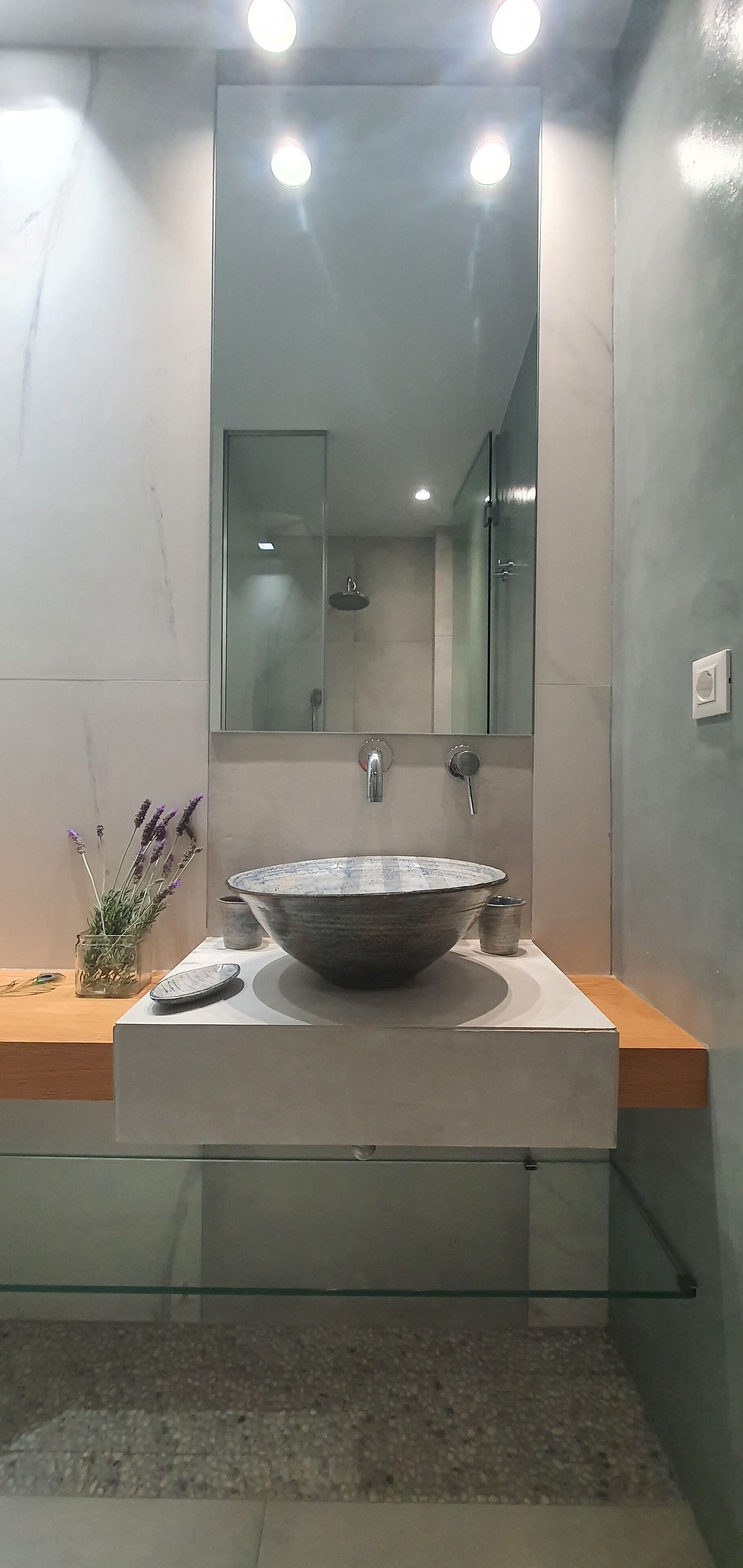 A modern bathroom with a large vessel sink, a glass shower enclosure, and a wooden vanity.