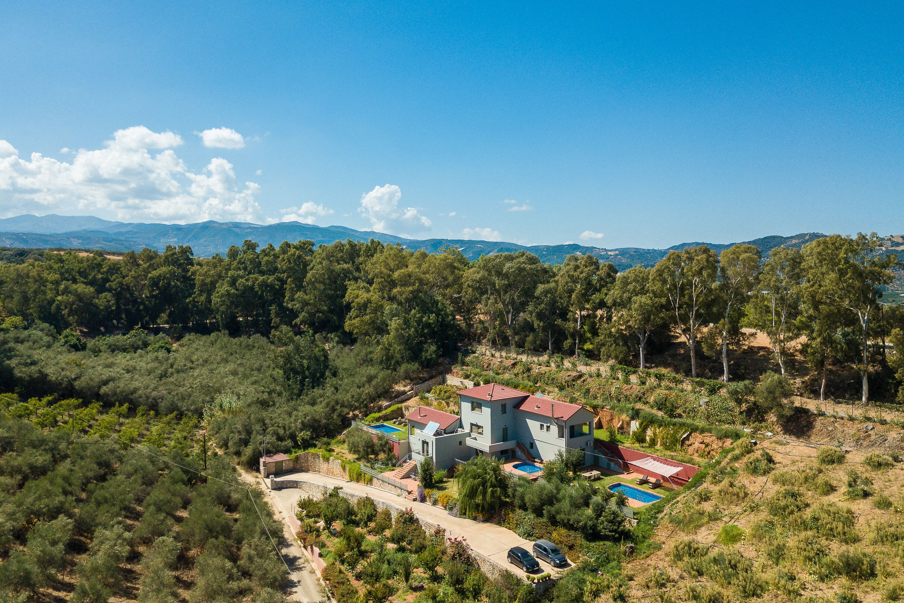 A modern two-story house with a swimming pool, surrounded by dense forest and hills in the background.