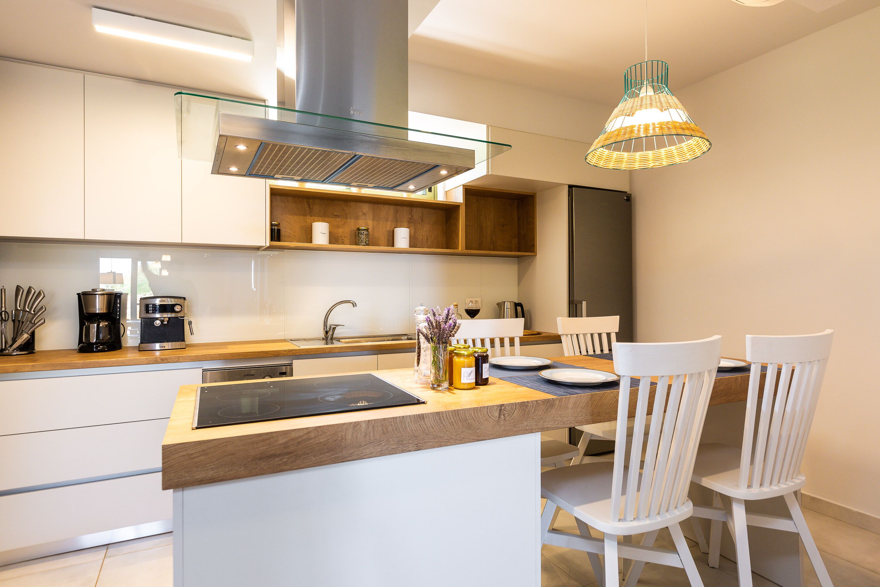A modern kitchen with a central island, white cabinetry, and a hanging light fixture.