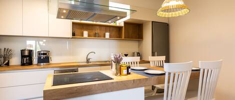 A modern kitchen with a central island, white cabinetry, and a hanging light fixture.