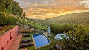 Piscina con sillones de descanso y una mesa, rodeada por un muro de piedra y abundante vegetación.