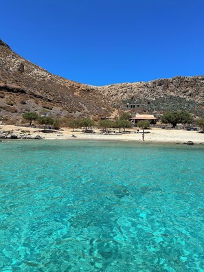 A coastal area with clear turquoise water, rocky hills, and a few buildings in the background. - Physis Villas Chania (Chania)