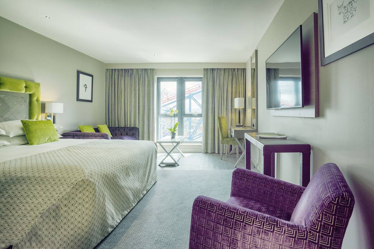 A hotel room with a bed, a desk, a chair, a window with curtains, and a view of a bridge.