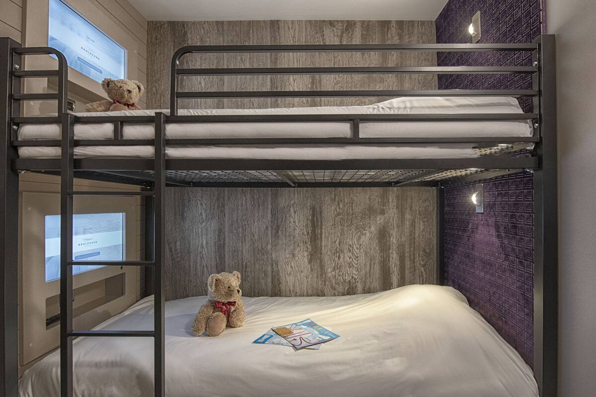 A bunk bed room with a wooden wall, a teddy bear on the lower bunk, and a TV screen on the left.