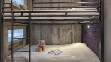 Een slaapkamer met stapelbed, een houten wand, een teddybeer op het onderbed en een televisiescherm aan de linkerkant.