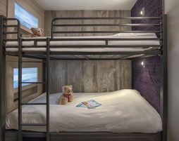 Een slaapkamer met stapelbed, een houten wand, een teddybeer op het onderbed en een televisiescherm aan de linkerkant.