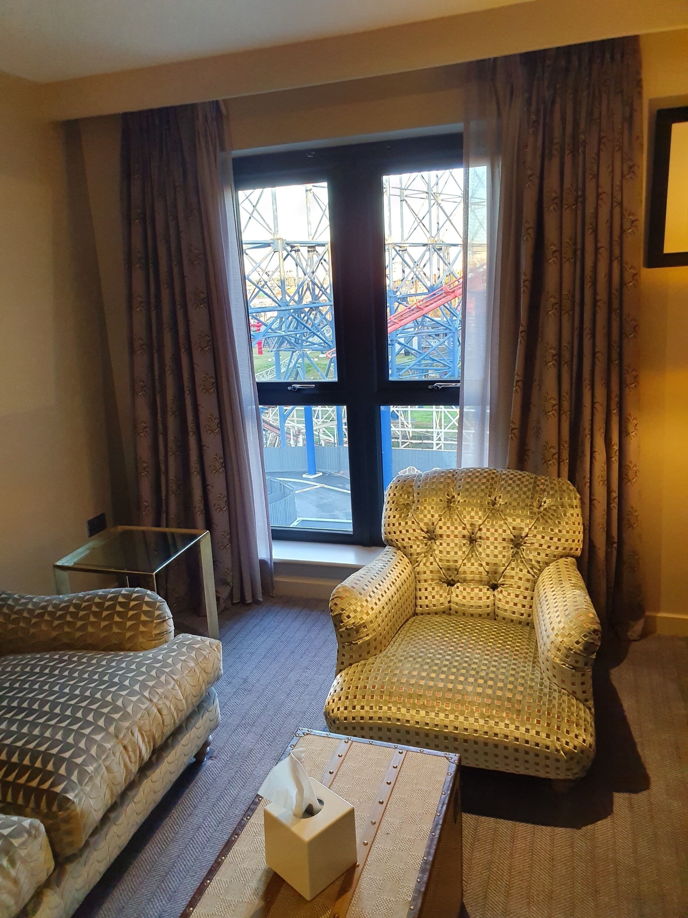 Una habitación de hotel con un ventanal grande, un sillón mullido, un sofá y una mesa de centro de vidrio.