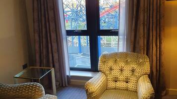 Una habitación de hotel con un ventanal grande, un sillón mullido, un sofá y una mesa de centro de vidrio.