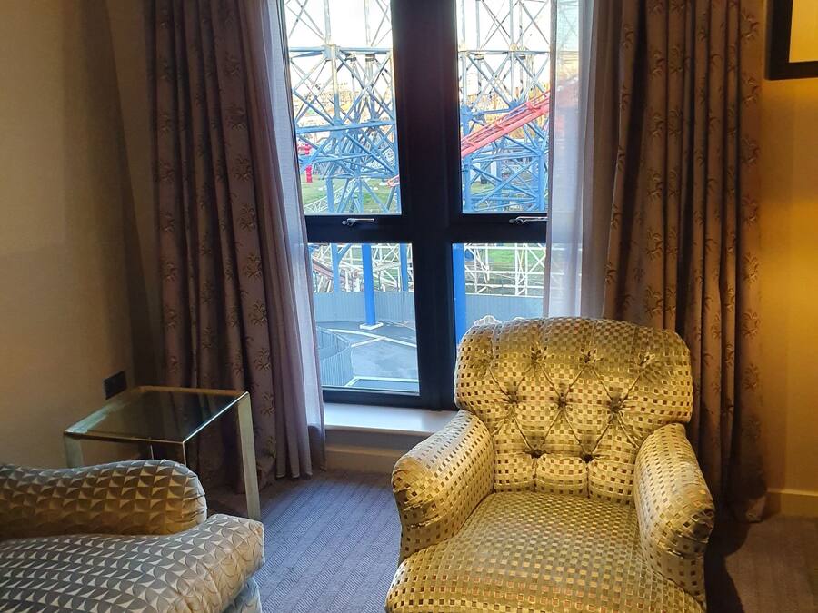 Una habitación de hotel con un ventanal grande, un sillón mullido, un sofá y una mesa de centro de vidrio.