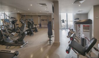 Een fitnessruimte met diverse trainingsapparaten, waaronder loopbanden, hometrainers en krachttrainingsmachines.